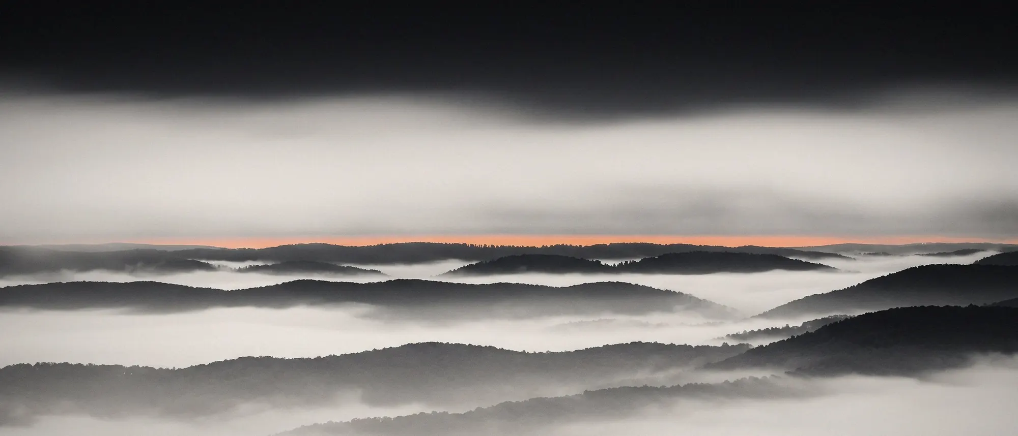 Ridgelines in morning fog with a thin band of sunrise at the horizon